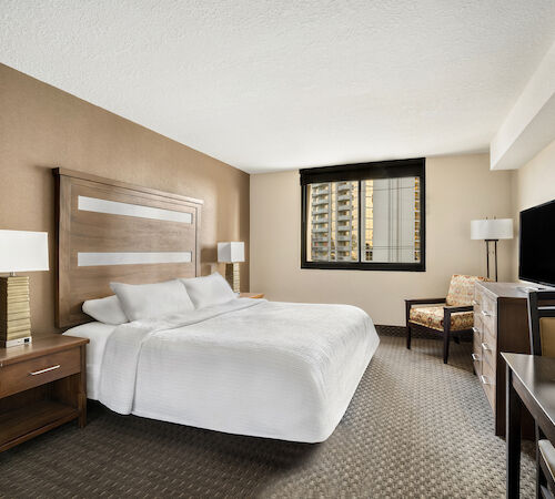 A hotel room with a large bed, two nightstands, a chair, and a TV