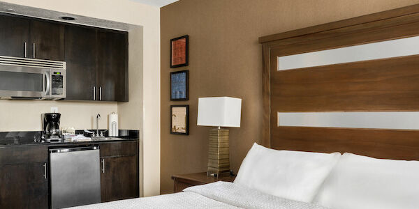 A hotel room with a king-sized bed, mini_fridge, microwave, and coffee maker.