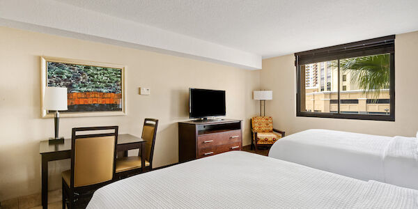 A hotel room with two beds, a desk, a TV, and a window.