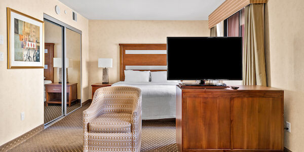 A wide view of a hotel room with a bed, TV, chair, mirror, and artwork.