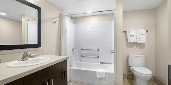 A clean bathroom with a sink, mirror, bathtub, toilet, and towels.