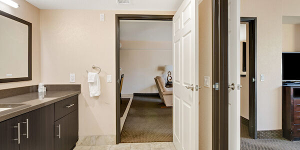 A hotel bathroom with a sink, mirror, and doorway to the room.