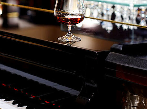 A glass of brown liquid sits on a piano at a bar.