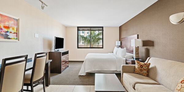 A hotel suite with a bed, sofa, TV, dining table, and window
