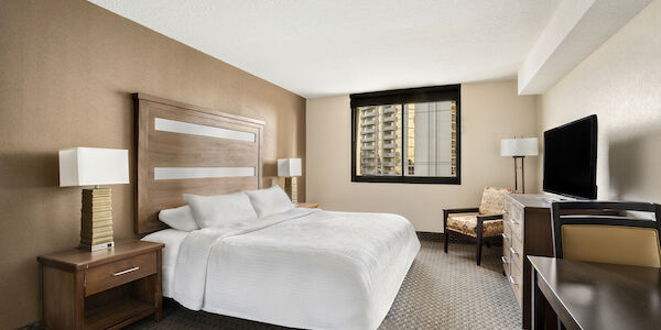 A hotel room with a large bed, two nightstands, a TV, and a window.