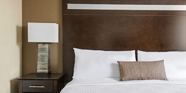 A close-up of a bed with a brown headboard, white bedding, and a nightstand with a lamp.