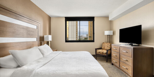 A hotel room with a large bed, dresser, TV, and chair