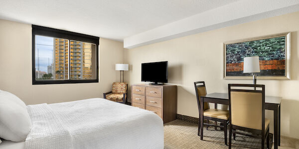A hotel room with a bed, TV, table, chairs, and artwork.