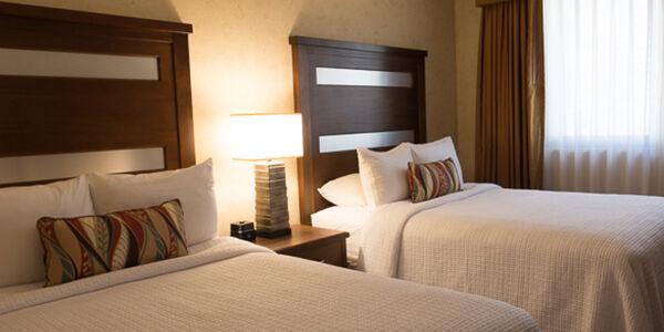 A hotel room with two beds, a nightstand, and a window.