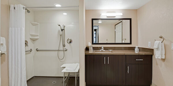 A bathroom with a shower, sink, mirror, and cabinet