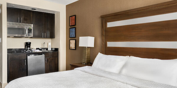 A hotel room with a kitchenette, bed, and artwork.