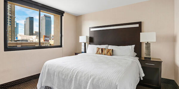 A hotel room with a large bed, two nightstands with lamps, and a window showing a city view.