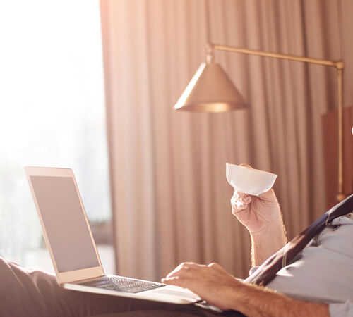 A person is sitting on a bed with a laptop and a cup of coffee.