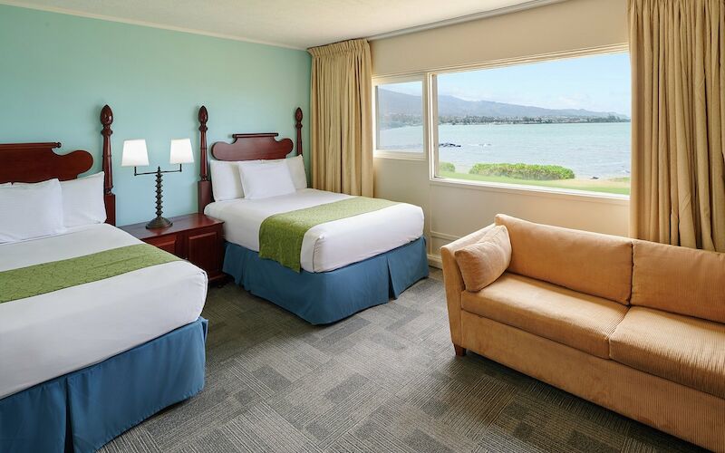 A hotel room with two beds, a sofa, and a window with a view.