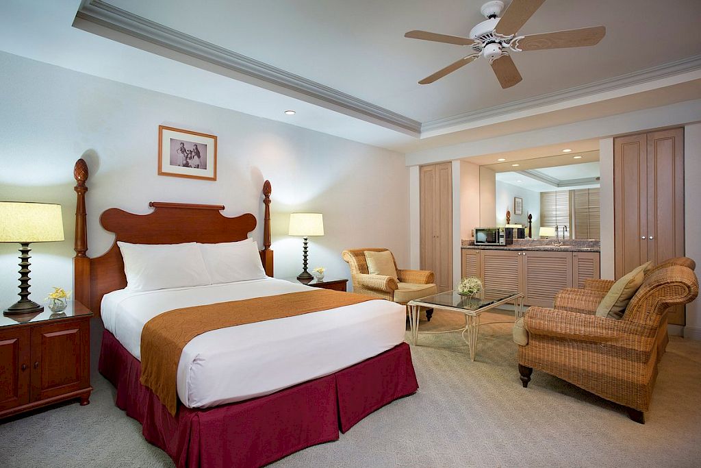 A hotel room with a bed, two nightstands, a sofa, and a kitchenette.