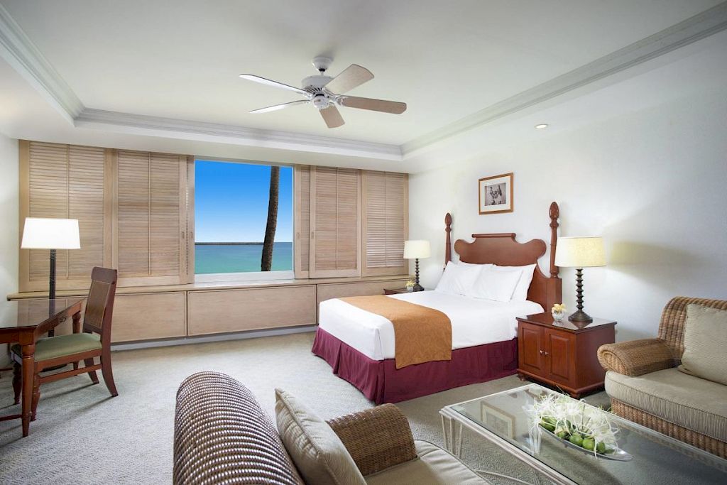 A wide view of a hotel room with a bed, sofa, desk, and ocean view.