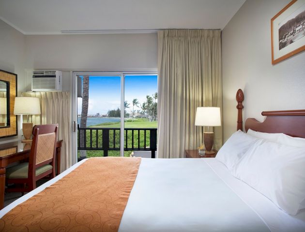 A hotel room with a bed, desk, and sliding glass door leading to a balcony with a view.